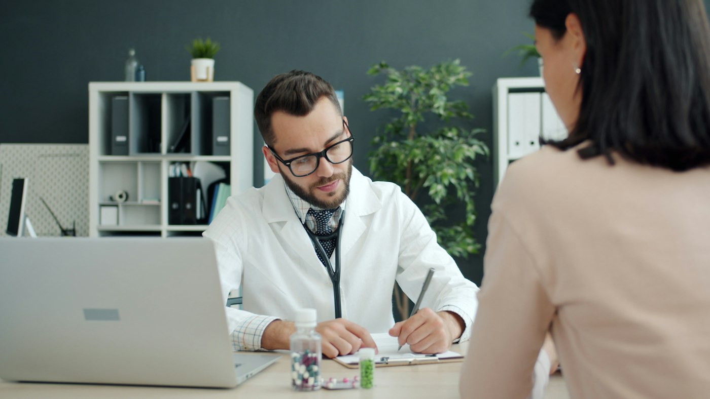 A doctor at his desk talking with a woman seated across from him