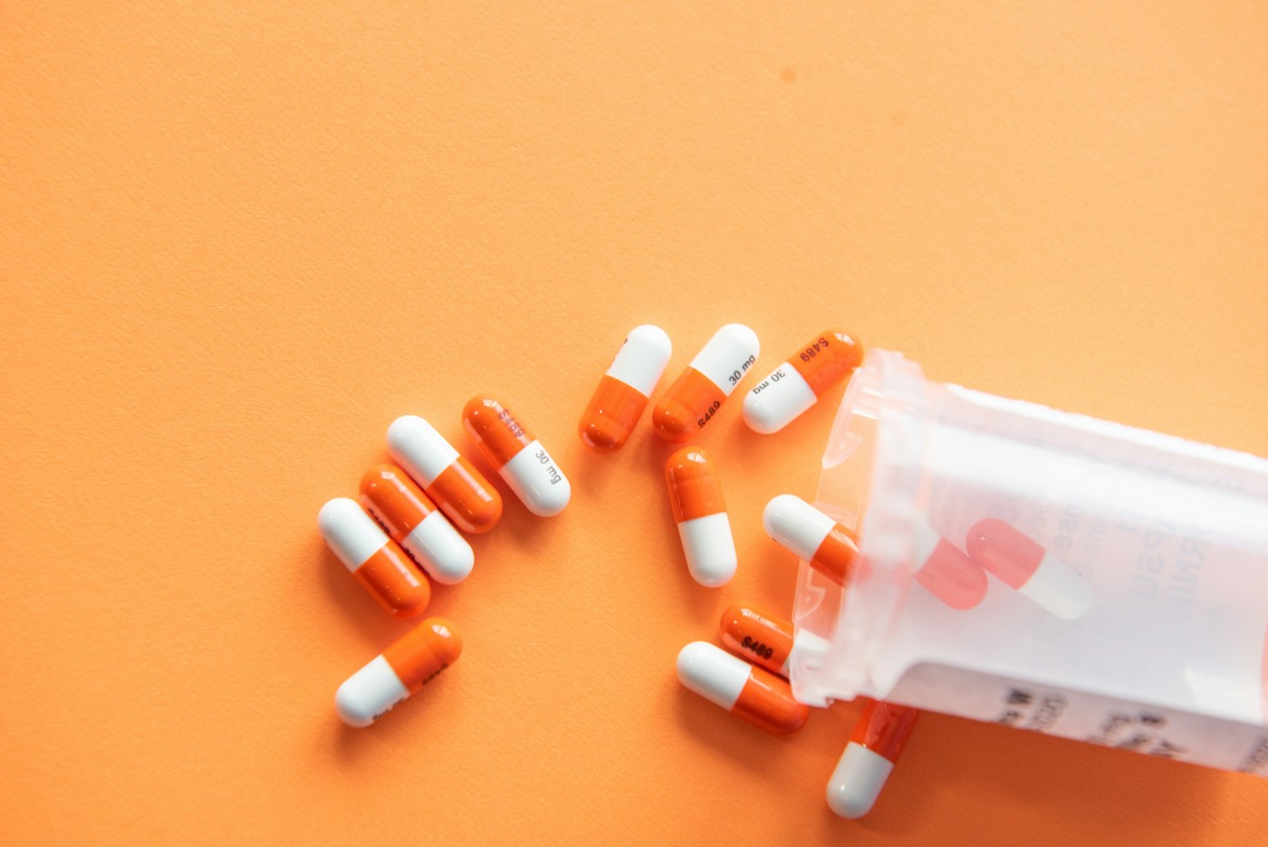 Orange and white capsules spilling from a pill bottle