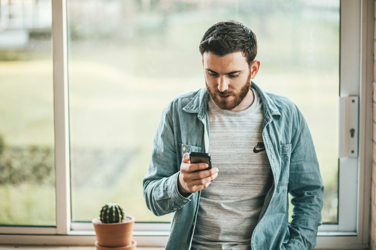 A man standing by a window reading a message on his phone